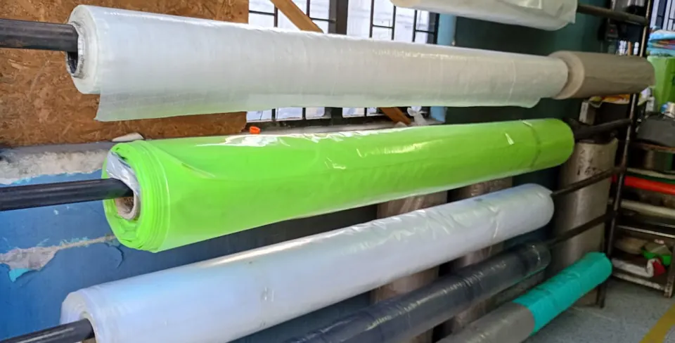 Rollos de plástico en un estante: transparente, verde y gris.